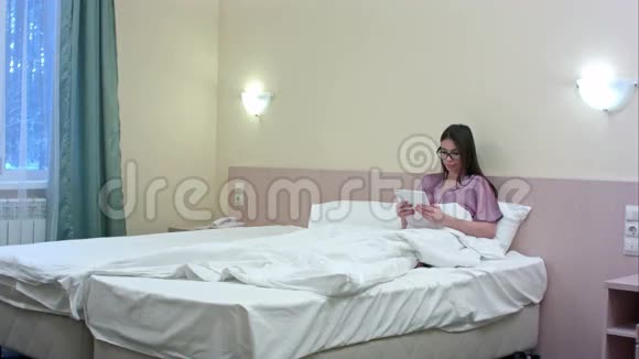 年轻的商务女性躺在酒店卧室里用平板电脑视频的预览图