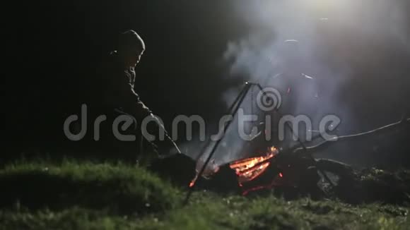 两个男孩晚上坐在篝火旁边纠正煤炭和交谈视频的预览图