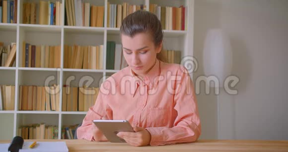 在大学图书馆的平板电脑上浏览的年轻有魅力女学生的特写照片视频的预览图