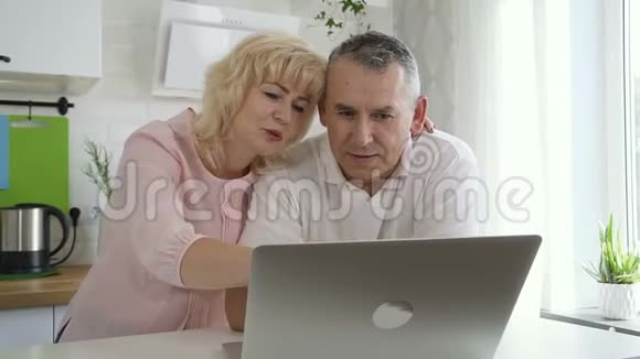 高级夫妻在公寓厨房里用电脑视频的预览图
