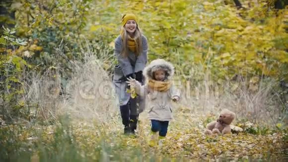 妈妈和她的女儿小女孩在秋天的公园里散步孩子跑慢动作视频的预览图