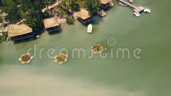 豪华山景酒店鸟瞰湖滨绿湖带茅草屋顶和船码头的夏季平房上的小屋视频的预览图