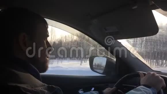 一个年轻的严肃男子正驾驶着一辆汽车在一条冬日的道路上在夕阳的照耀下1920x1080视频的预览图