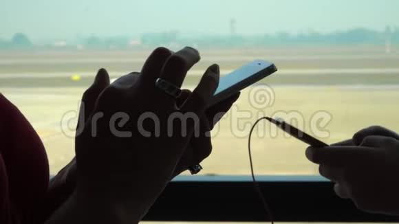 在机场窗口用信使或智能手机输入短信的女性手的特写镜头两个女孩站着视频的预览图