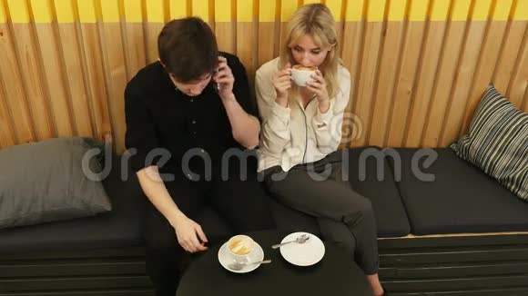 年轻人一边和女朋友坐在咖啡馆里用手机打电话视频的预览图