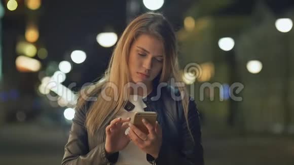 金发女人晚上在城市里用手机视频的预览图