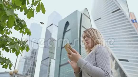 美丽的金发女孩在市中心的背景下使用手机视频的预览图