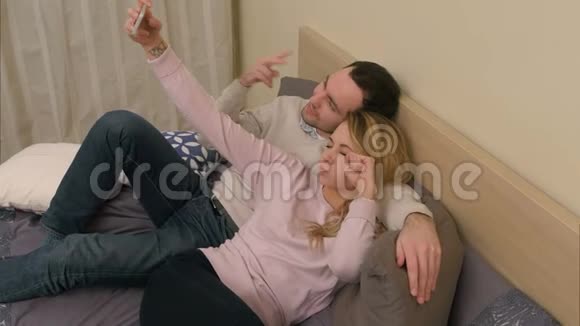 年轻夫妇用手机拍自拍照片躺在家里的卧室里视频的预览图