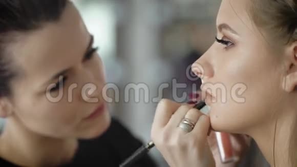 经验丰富的化妆师很快就用高质量的化妆铅笔把女孩的嘴唇涂上专业人员视频的预览图