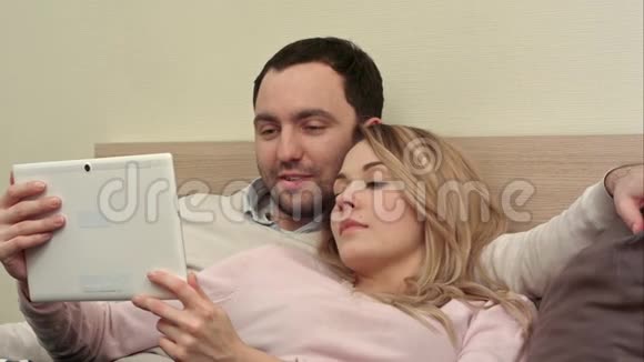 躺在床上的年轻夫妇用平板电脑上网购物视频的预览图