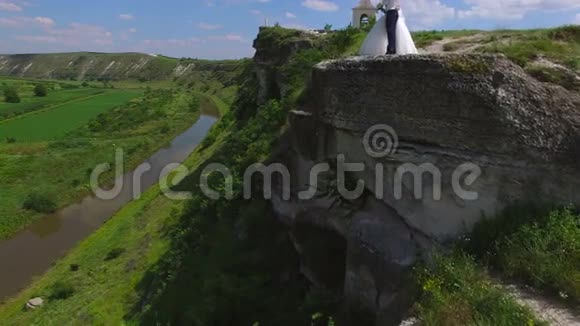 站在河边悬崖上的新婚夫妇的鸟瞰图视频的预览图