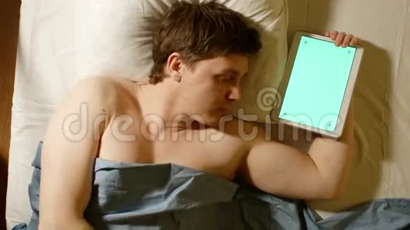 白人年轻人睡觉手拿平板电脑绿色屏幕视频的预览图