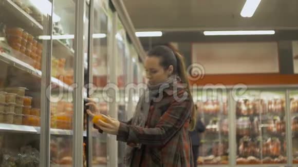 年轻女子在超市购物打开冰箱去取冷藏食品视频的预览图