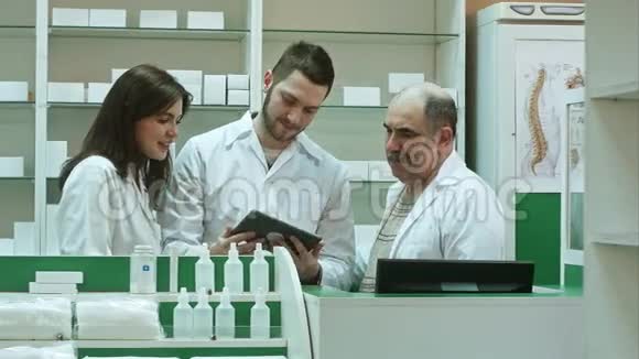 在药房柜台使用平板电脑的三名药剂师视频的预览图