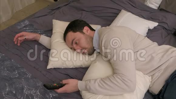 疲倦的人躺在床上休息用遥控器看电视视频的预览图