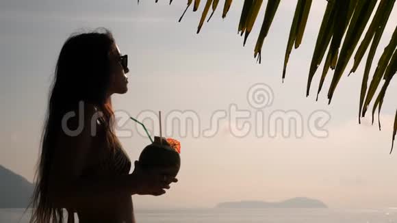 在热带海滩喝新鲜泰国椰子水鸡尾酒的年轻旅游妇女剪影4K慢动作普吉岛视频的预览图