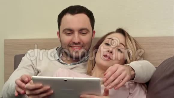 年轻夫妇在床上使用数码平板电脑笑着笑着视频的预览图