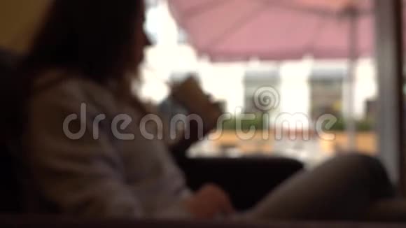 在靠窗的咖啡馆里用吸管喝饮料的发散的黑发女孩慢动作背景bokeh镜头视频的预览图