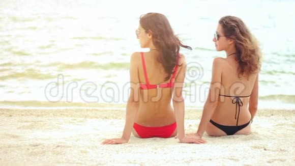 穿着泳装坐在沙滩上的女性的后景视频的预览图