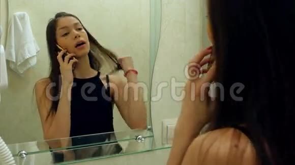 女人梳头梳头通过智能手机在酒店浴室与她的朋友交谈视频的预览图