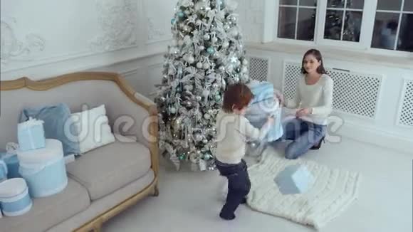 妈妈和她的小儿子把礼物放在圣诞树下视频的预览图