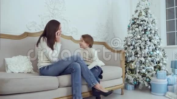 年轻的母亲在手机上聊天而她的儿子在玩视频的预览图