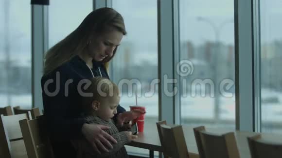 妈妈和儿子坐在咖啡馆里妈妈看起来像个儿子坐在电话里视频的预览图