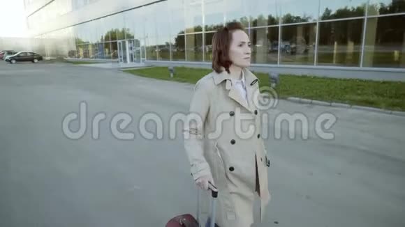 一个女人带着手提箱走到机场大楼一位商务女士带着一个轮子的手提箱走到停车场视频的预览图