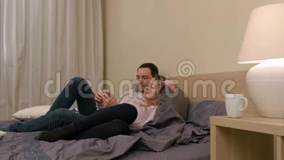 爱的夫妇坐在床上用智能手机讨论新照片视频的预览图