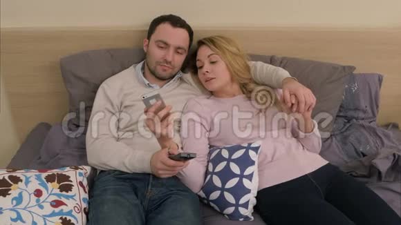 坐在床上用智能手机触摸屏微笑着看旅行照片的漂亮夫妇视频的预览图