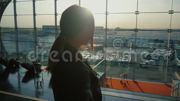 年轻女子正在等待航班一扇大窗户背景下的剪影视频的预览图