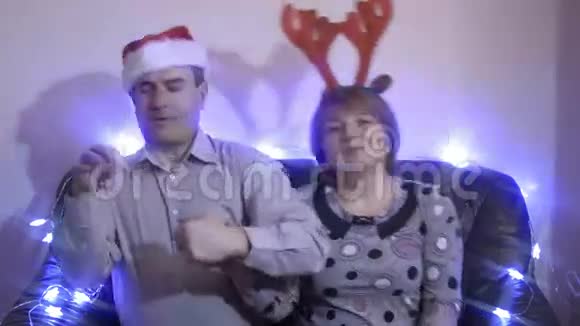 戴着圣诞帽和驯鹿角的中年夫妇坐在沙发上跳舞视频的预览图