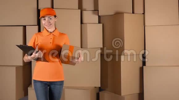 穿着橙色制服的漂亮的女快递员把一个包裹靠在纸板箱后面4K工作室视频视频的预览图