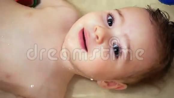 可爱的小女婴躺在浴缸里看着镜头视频的预览图