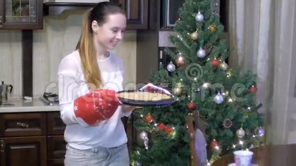 年轻的女人闻着烤馅饼的味道戴着手套把它放在了圣诞节的背景上视频的预览图