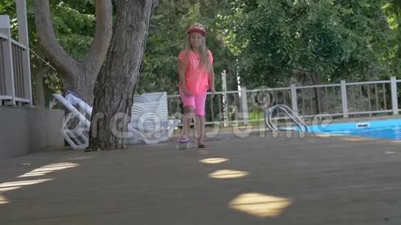 可爱的金发小女孩在游泳池边的滑板上滑冰视频的预览图