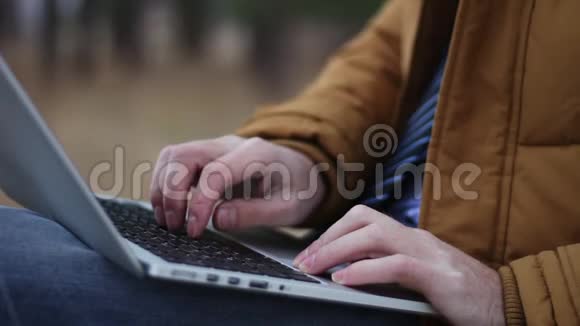 坐在长凳上的公园里人手在笔记本电脑键盘上打字视频的预览图