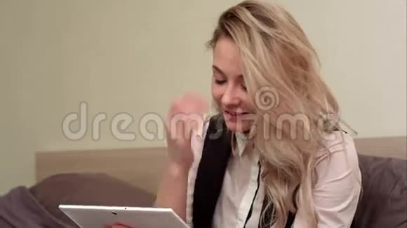 兴奋的微笑着的女人坐在床上一边在平板电脑上打视频电话视频的预览图