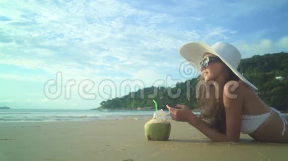 海滩上穿着游泳衣喝着椰子鸡尾酒的女人视频的预览图