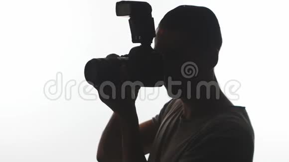 摄影师特写的剪影年轻人用白色背景的数码单反相机拍照视频的预览图