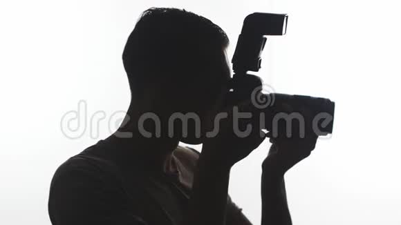 摄影师剪影特写年轻人用白色背景的数码单反相机拍照视频的预览图