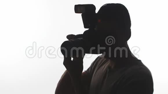 摄影师特写的剪影年轻人用白色背景的数码单反相机拍照视频的预览图