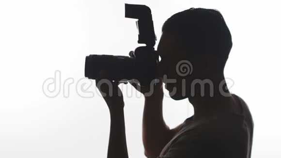 摄影师剪影特写年轻人用白色背景的数码单反相机拍照视频的预览图