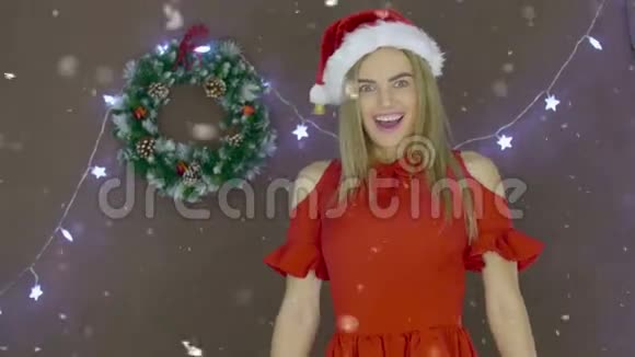 可爱的年轻女性穿着红色连衣裙和圣诞帽在圣诞节背景下亲吻你视频的预览图