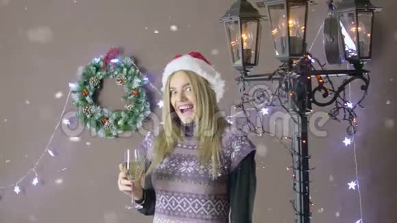 漂亮的金发女孩戴着圣诞帽手里拿着一杯香槟和一个写着圣诞快乐的酒杯视频的预览图