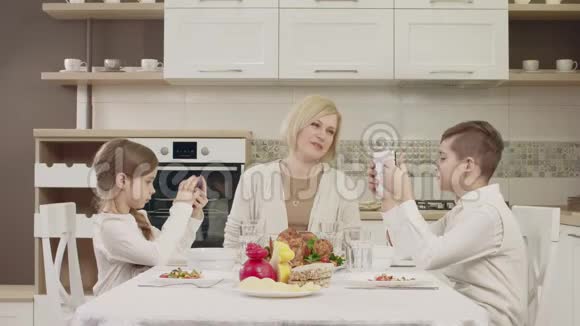 妈妈在家庭聚餐时和孩子们在桌边交流视频的预览图
