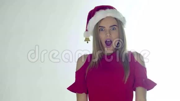 一个穿着红色圣诞帽手持床单在白色背景上露出惊讶笑容的圣诞妇女视频的预览图