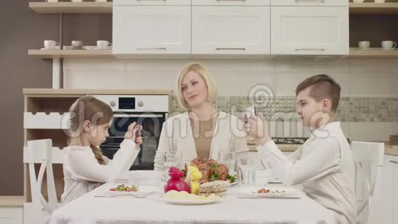 妈妈在家庭聚餐时和孩子们在桌边交流视频的预览图