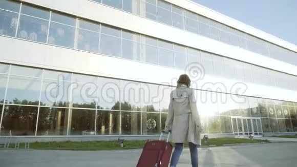 一个女人带着手提箱走到机场大楼一位商务女士带着一个轮子的手提箱走到停车场视频的预览图