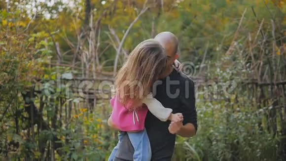 爸爸抱在怀里爸爸和女儿在秋天的公园里玩旋转和跳舞的乐趣慢动作视频的预览图